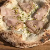 Pizza Napoletana mit Mortadella, Pistazien und cremiger Füllung auf einem Holzbrett.