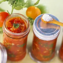 Frische Tomaten und Gläser mit Tomaten-Salsa, perfekt für leckere Tomaten Rezepte. Eine Löffelspitze Salz liegt bereit.