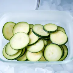 Scheiben von Zucchini lagern in einem Glasbehälter auf Eiswürfeln.