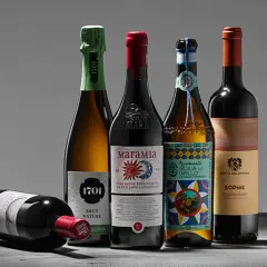 Fünf Flaschen Wein, darunter ein Sekt und vier Rotweine, stehen auf einem Tisch. Einer der Rotweine liegt. Ein Etikett weist auf biodynamischen Wein hin.