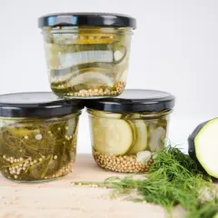Drei Gläser mit eingelegtem Gemüse, bereit zum Einkochen im Weckglas. Zucchini, Zwiebeln und Dill sind mit Senfkörnern gefüllt.