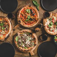 Vier leckere Pizzen, ein Salat und Rotwein auf rustikalem Holztisch. Perfekt für einen gemütlichen Abend mit Freunden.