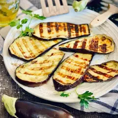 Gegrillte Aubergine-Scheiben mit Grillstreifen, garniert mit Petersilie, daneben Salz und Öl.