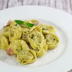 Spinat Ricotta Tortellini in cremiger Sauce, garniert mit Basilikum und schwarzem Pfeffer. Ein köstliches Gericht, das zum Genießen einlädt.