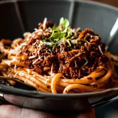 Eine Schüssel mit herzhaftem Pasta Ragu, garniert mit frischen Kräutern und geriebenem Käse.