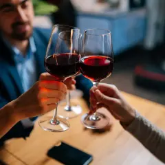 Drei Personen stoßen mit Rotwein an. Sie halten das weinglas richtig, am Stiel, um die Temperatur des Weins zu bewahren.