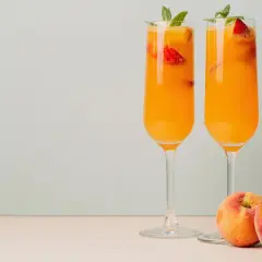 Zwei Bellini-Cocktails mit Pfirsich und Erdbeeren, garniert mit Minze. Das Bellini Rezept original ist einfach und erfrischend.