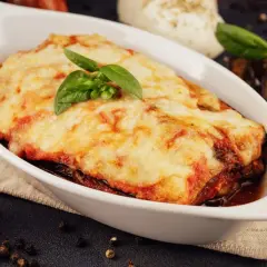 Herzhafte Auberginen Lasagne mit geschmolzenem Käse und frischem Basilikum, serviert in einer weißen Auflaufform.