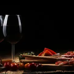 Zwei Gläser Rotwein, ein Cuvee Wein, stehen neben einer rustikalen Platte mit Käse, Schinken, Brot und Oliven.