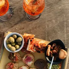 Zwei Aperol Spritz und eine Auswahl an italienischen Aperitif-Spezialitäten: Oliven, Bruschetta und Pizza.