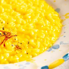Cremiges, gelbes Risotto Milanese, garniert mit Safranfäden und schwarzem Pfeffer, in einem handbemalten Teller.