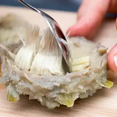 Mit einer Gabel werden die faserigen Teile einer Artischocke entfernt. So kann man Artischocken zubereiten.