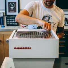 Mann reinigt eine La Marzocco Espressomaschine. Sorgfältige Pflege für perfekten Kaffeegenuss.