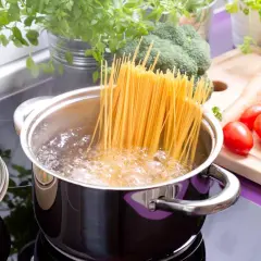 Spaghetti kochen in sprudelndem Wasser. Die genaue Zeit, wie lange nudeln kochen, hängt von der Sorte ab. Frische Kräuter und Gemüse liegen bereit.