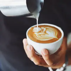 Ein Barista gießt Milch in eine Tasse, um ein Latte Art Muster zu kreieren. Ein perfekter Kaffee auf italienisch.