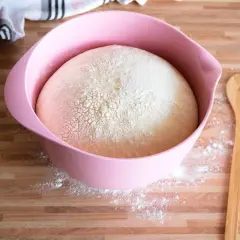 Ein aufgegangener Hefeteig in einer rosa Schüssel, bereit für die Zubereitung. Daneben liegt ein Holzlöffel mit Herz.