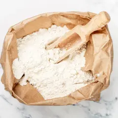 Eine Papiertüte mit Mehl, bereit zum Lagern, mit einer Holzschaufel darin.