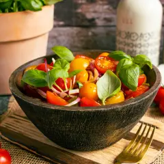 Frischer Tomatensalat italienisch mit Basilikum, Zwiebeln und Kirschtomaten in einer Holzschale.