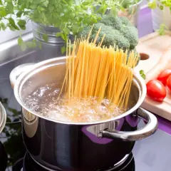 Spaghetti kochen: Lange Nudeln im sprudelnden Wasser, daneben frisches Gemüse wie Brokkoli, Tomaten und Salat.