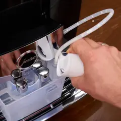 Hand füllt Entkalkungsmittel in eine Jura Kaffeemaschine. Regelmäßiges Entkalken sorgt für Langlebigkeit.