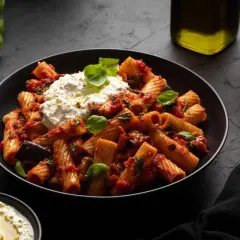 Rigatoni mit Auberginen-Tomaten-Sauce und cremigem Ricotta – ein Beweis für die besten Rezepte mit Auberginen. Frischer Basilikum und Olivenöl runden das Gericht ab.