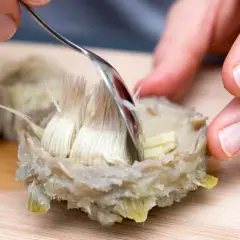 Mit einer Gabel wird das zarte Herz einer gekochten Artischocke freigelegt. So isst man Artischocken: Blatt für Blatt abziehen und das Fleisch abkratzen.