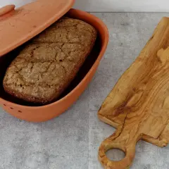 Ein Laib Brot liegt in einem Terrakotta-Brotbehälter. Daneben eine Holzschneidebrett. Perfekt, um Brot aufbewahren.