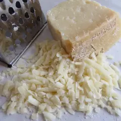 Ein Stück Pecorino liegt neben frisch geriebenem Käse und einer Reibe. Der Kampf Pecorino vs Parmesan beginnt!