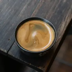 Ein dampfender americano kaffee mit schöner Crema in einer dunklen Tasse auf einem rustikalen Holztisch.