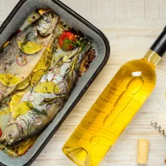Zwei gebackene Forellen mit Zitrone und Kräutern, daneben eine Flasche Weißwein und ein Glas. Perfekt, welcher Wein zu Fisch passt!