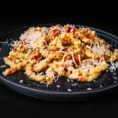 Gedrehte Pasta mit Pesto Trapanese, Tomaten und geriebenem Käse auf einem dunklen Teller.