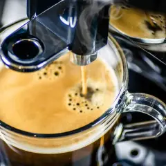 Frisch gebrühter Espresso fließt aus einem Vollautomaten in eine Glas Tasse. Der Kaffee schmeckt bitter, aber die Crema ist perfekt.