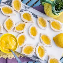 Zitronenkekse italienisch, mit leuchtend gelber Zitronencreme gefüllt und mit Puderzucker bestäubt, liegen auf einem Marmorbrett.