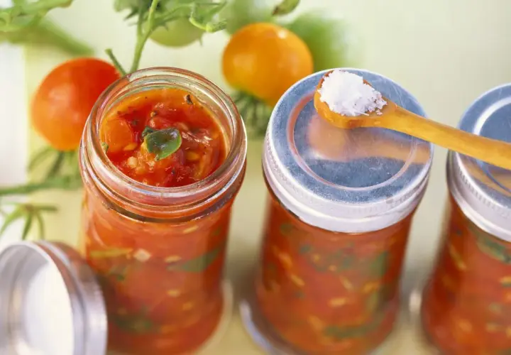 Frische Tomaten und Gläser mit Tomaten-Salsa, perfekt für leckere Tomaten Rezepte. Eine Löffelspitze Salz liegt bereit.