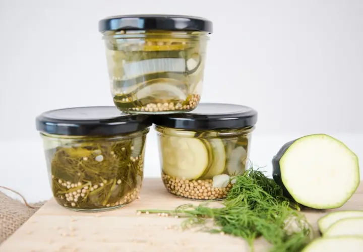 Drei Gläser mit eingelegtem Gemüse, bereit zum Einkochen im Weckglas. Zucchini, Zwiebeln und Dill sind mit Senfkörnern gefüllt.