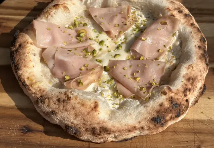 Pizza Napoletana mit Mortadella, Pistazien und cremiger Füllung auf einem Holzbrett.