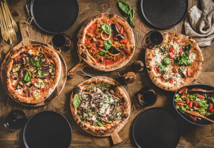 Vier leckere Pizzen, ein Salat und Rotwein auf rustikalem Holztisch. Perfekt für einen gemütlichen Abend mit Freunden.