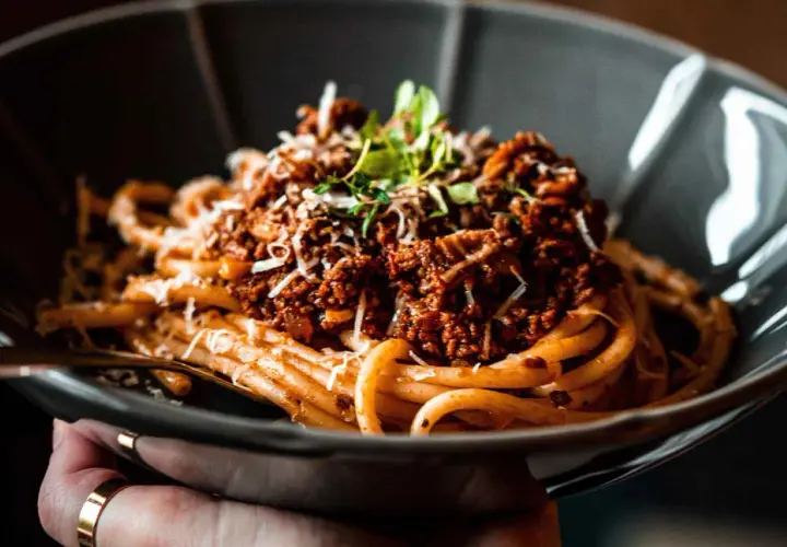 Eine Schüssel mit herzhaftem Pasta Ragu, garniert mit frischen Kräutern und geriebenem Käse.