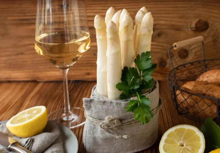 Ein Glas Weißwein neben frischem Spargel, Kartoffeln und Zitronen. Die perfekte Kombination, um die Frage zu beantworten: welchen Wein zu Spargel.