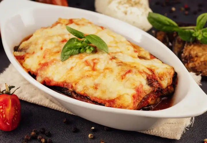 Herzhafte Auberginen Lasagne mit geschmolzenem Käse und frischem Basilikum, serviert in einer weißen Auflaufform.