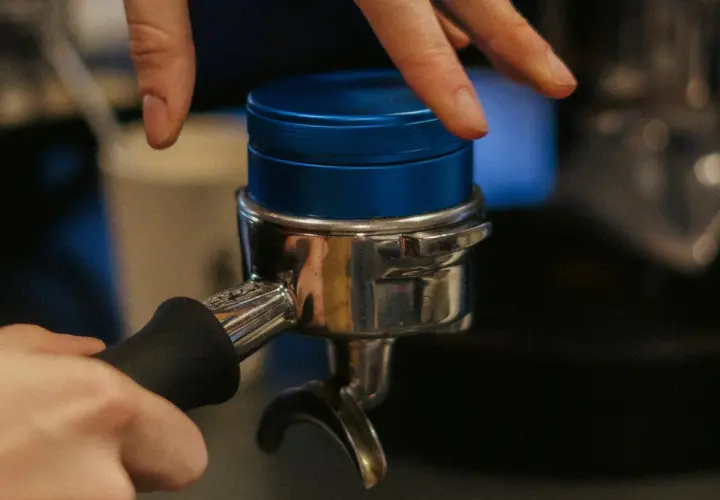 Barista bereitet Espresso zu, indem er den Tamper auf den Kaffeepuck im Siebträger drückt.