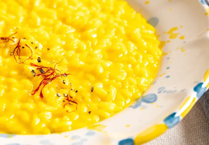 Cremiges, gelbes Risotto Milanese, garniert mit Safranfäden und schwarzem Pfeffer, in einem handbemalten Teller.