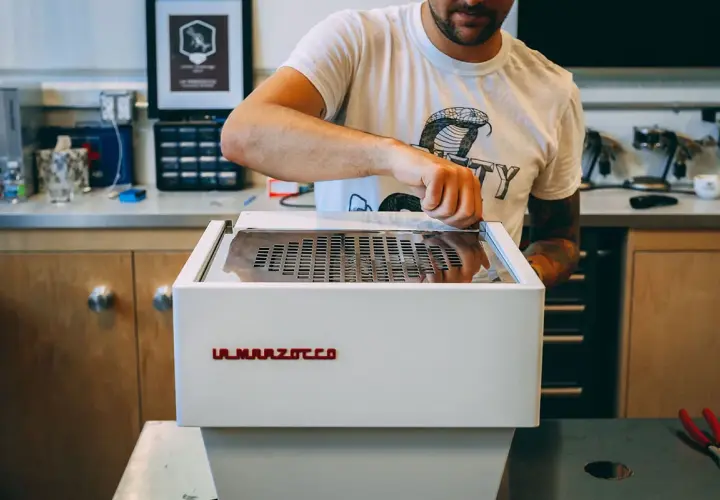 Mann reinigt eine La Marzocco Espressomaschine. Sorgfältige Pflege für perfekten Kaffeegenuss.