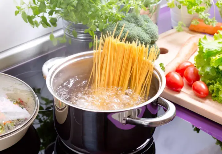 Spaghetti kochen in sprudelndem Wasser. Die genaue Zeit, wie lange nudeln kochen, hängt von der Sorte ab. Frische Kräuter und Gemüse liegen bereit.