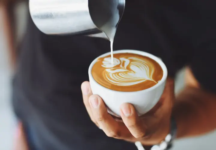 Ein Barista gießt Milch in eine Tasse, um ein Latte Art Muster zu kreieren. Ein perfekter Kaffee auf italienisch.
