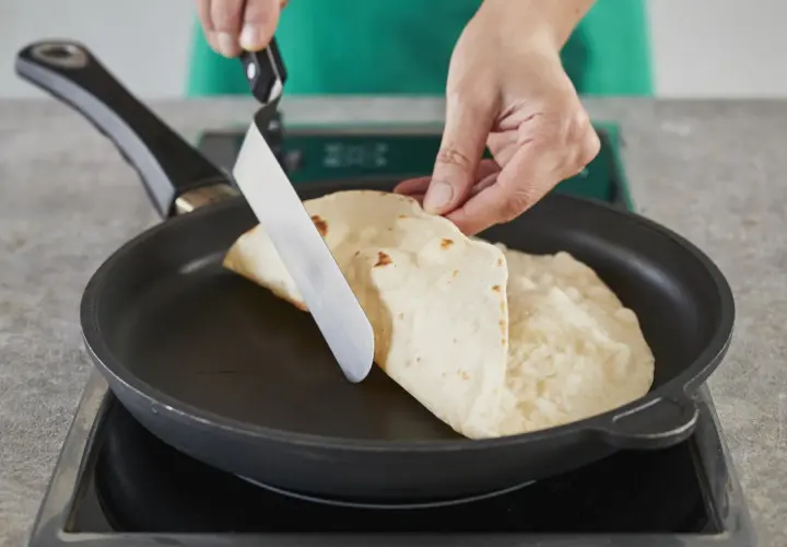 Hände falten Piadinas in einer Pfanne für ein einfaches Piadina Rezept.
