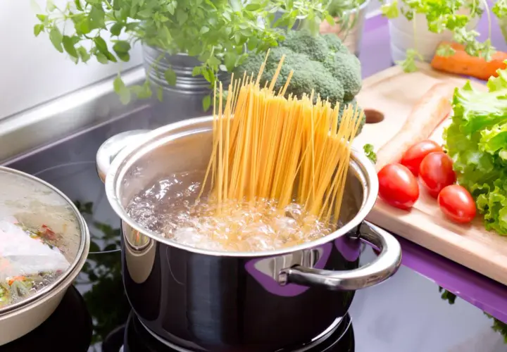 Spaghetti kochen: Lange Nudeln im sprudelnden Wasser, daneben frisches Gemüse wie Brokkoli, Tomaten und Salat.