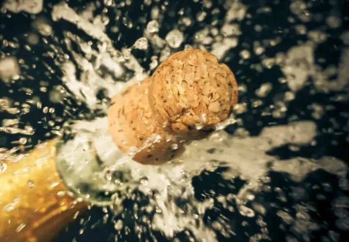 Champagnerkorken spritzt aus der Flasche, ein Moment des Feierns, der zeigt, wie wichtig es ist, Champagner richtig zu lagern.
