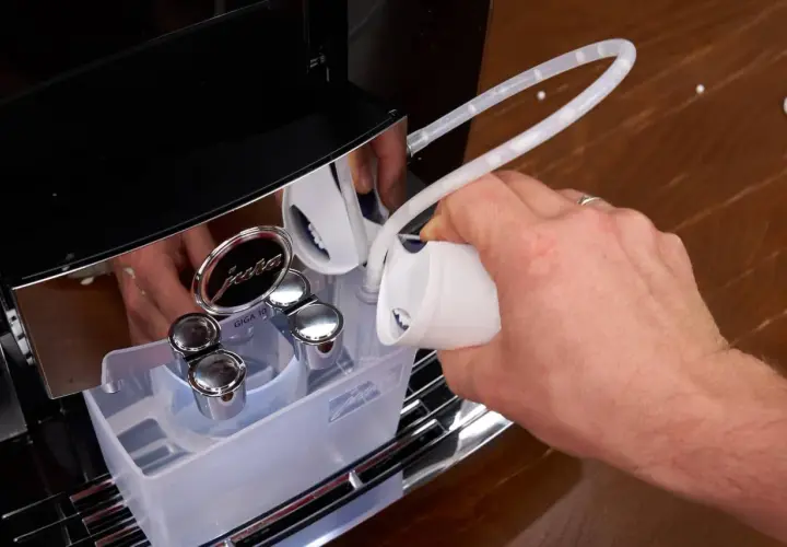 Hand füllt Entkalkungsmittel in eine Jura Kaffeemaschine. Regelmäßiges Entkalken sorgt für Langlebigkeit.
