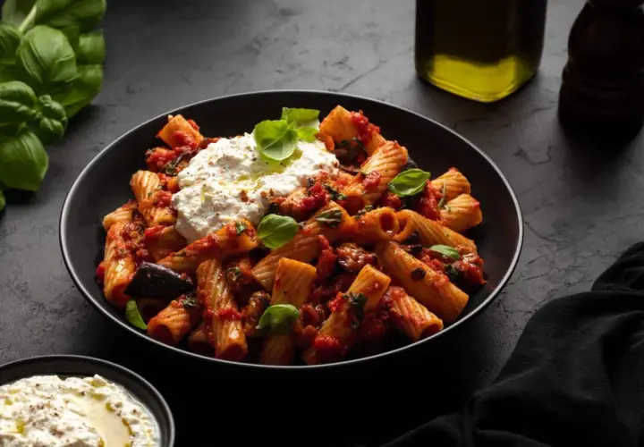 Rigatoni mit Auberginen-Tomaten-Sauce und cremigem Ricotta – ein Beweis für die besten Rezepte mit Auberginen. Frischer Basilikum und Olivenöl runden das Gericht ab.